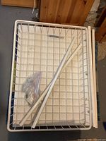 Photo of white metal wire basket frame with two support rails and mounting hardware on top, illustrating storage basket and hardware components.