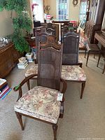 Photo showing two captain chairs with armrests and four armless chairs behind them, all with floral upholstered seats and woven cane backs featuring decorative wood carvings
