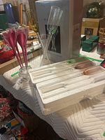 Set of colorful Mantle champagne stem glasses arranged in a clear vase, some lying on a padded white cloth, with 4 Moet & Chandon clear champagne flutes also visible on the side.