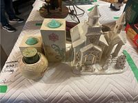 Front view of ceramic candle holders, decorative container and ceramic church figurine with Christmas tree detail.