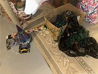 Box containing several strands of green wire Christmas string lights, New Year party hats, and sparklers visible nearby on floor.