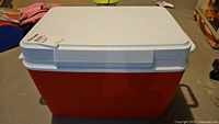 Front angle view of the Rubbermaid cooler showing red base and white lid with handle.