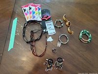 Photo showing various bracelets, clip-on earrings with bead and feather details, tortoiseshell and black hair bands, costume ring, gold-tone brooch, and colorful bow-shaped hair clips arranged on wooden surface.