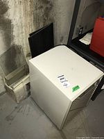 White Simplicity 28 Frostguard dehumidifier with front vents and a single dial, placed on a concrete basement floor near a stack of tiles and glass sheets.