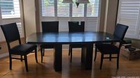 Full view of large wooden dining table with four chairs around it, table has dark two tone finish and block legs
