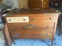 Front view of vintage wooden dresser with four drawers, one drawer unfinished and missing stain or finish. Drawer hardware varies with standard knobs and drop pulls. Top drawer has a lighter natural wood finish compared to the rest of the dresser.