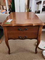 Front view of wood end table showing two drawers with decorative metal handles and curved legs.