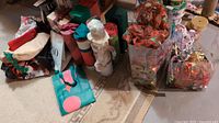 Wide view of various Christmas gift bags, bottle gift bags, gift boxes, and wrapped ribbons arranged on a carpeted floor.