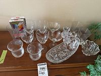Full overview of the glassware including stemware, rocks glasses, candy bowls, candleholders, bud vase, and wine glass markers on a wooden surface against a plain wall.