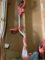 Full view of Grass Hog electric grass trimmer showing orange and gray curved shaft with auxiliary handle and trigger grip.