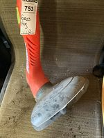 Photo of orange Grass Hog string trimmer showing side view of shaft and plastic guard with visible dirt and wear.