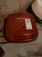 Red George Foreman grill seen from above showing lid and power cord with seller label.
