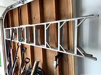 Full length view of the 12-foot aluminum step ladder leaned against a wooden wall, showing the entire ladder and its structure.