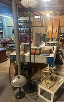 Two lamps side by side in basement setting; one short table lamp with frosted shade, one tall floor lamp with white glass shade.