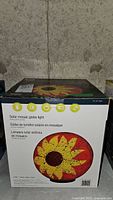 Front of box showing image of solar mosaic globe light with sunflower design and basic product information in English, French, and Spanish.