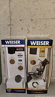 Photo of two Weiser lock boxes, one with a deadbolt lock and the other with a door handle lock set, both partially assembled inside the packaging.