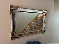 Full view of the rectangular mirror mounted on a wall, showing its reflective surface and gold accented frame.