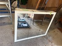 Front angle of white framed manufactured wood cabinet with three mirrored doors on floor in a garage setting.
