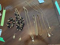 Overview of all jewelry items on a wooden surface including multi-strand bead necklaces, bracelet, chain necklaces, and earrings