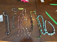 Eight beaded necklaces displayed on a table including hematite and multicolored beads.