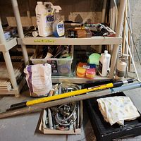 Overview of multiple paint supplies on metal shelving in basement including bottles, brushes, rollers, grout and other accessories