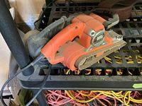 Photo of the Black & Decker dragster sander resting on a metal shelf with extension cords below.