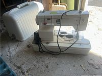 Simpsons sewing machine next to white plastic carrying case, shown on garage floor.