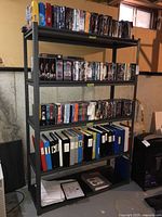 Front view of the metal shelving unit filled with DVDs and binders, showing five shelves and sturdy frame.