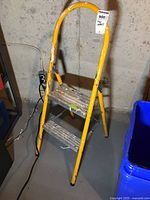 Front view of yellow metal step ladder showing two metal steps with paint stains and curved handle.