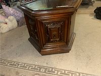 Side angled view of hexagonal wood cabinet showing carved panel design and scratches on surface.