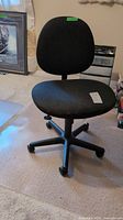 Front view of black fabric task office chair with castor wheels on carpet.