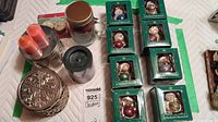 Photo of eight boxed The Boyds Collection Christmas tree ornaments in green packaging, three cylindrical candles, two LED tealights, and two decorative metal boxes with embossed snowflake design