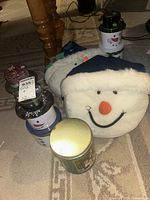 Three snowman tins and one plush snowman pillow on floor under table