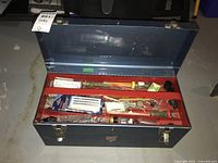 Blue metal toolbox open to show red tray compartments filled with various hand tools and accessories including a metal saw.