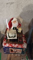 Front view of the animated Santa figurine sitting at a wooden desk holding a quill pen and inkwell, with Christmas scroll and gift.