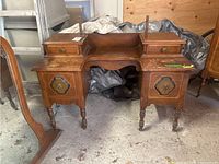 Front angle view of vintage wood vanity showing drawers and turned legs, placed on concrete floor with some surrounding items.