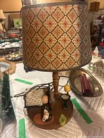 Side view of vintage lamp showing detailed fabric lampshade with diamond floral pattern and miniature decorative items on wooden base.