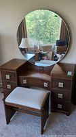 Front view of vintage wood vanity with large round mirror and upholstered bench seat.