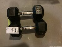 Pair of two black hexagonal 25 lb dumbbells on concrete floor showing weight markings and metal handles.