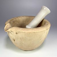 Porcelain mortar with marble pestle inside showing surface wear and chips