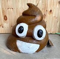 Front view of the large poop emoji fiberglass sculpture showing face with eyes and smile, some minor surface marks and wear.