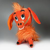 Front view of the orange plush donkey toy from 1967 with facial details, gold harness, and fluffy fur around neck and back, sitting pose.