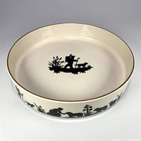 Top view showing interior with central black silhouette of a man with dog and grass on cream background, gold rim visible.