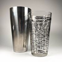 Photo showing the stainless steel cocktail shaker cup next to the clear glass insert with printed vintage cocktail recipes and measurement markings.