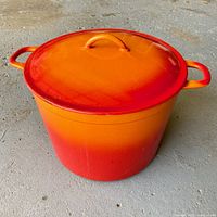 Photo of the closed vintage Descoware flame orange enamel Dutch oven showing gradient colors and handles.