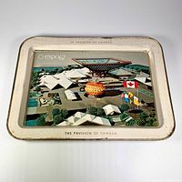 Front view of rectangular metal tray featuring aerial photo of Expo 67 Canada Pavilion, bilingual French and English text, and flags.