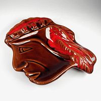 Top-view photo of the ceramic ashtray shaped like a stylized Indigenous head profile with red and white drip glaze detail on the headdress and face.