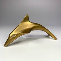 Photo showing the dolphin figurine from a side angle highlighting its smooth brass finish and shape with a pointed nose and fin details.
