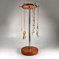 Front view of vintage necklace display stand with four necklaces hanging from six hooks on the wooden top disk, supported by a chrome central rod and wooden round base.