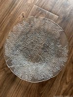 Top-down view of clear glass plate with textured fern leaf pattern on wooden surface.